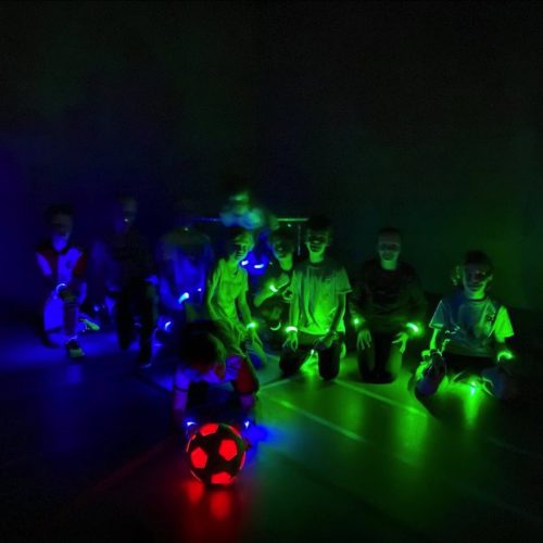 LED Voetbal Rotterdam. Kinderen in LED bandjes in een verduisterde gymzaal, klaar om te beginnen.